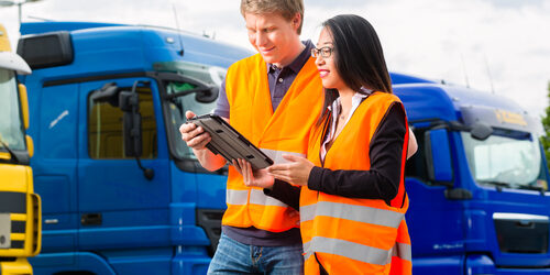 man and woman on tablet device in front of a truck fleet