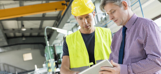 two men on a construction site looking at a tablet device