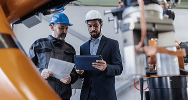 Two men in hard hats look onto a tablet.